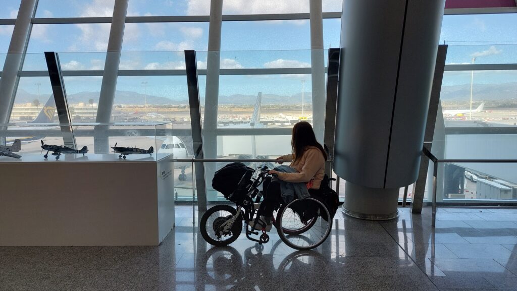 Person in a wheelchair and Batec handbike waiting at the airport before boarding a plane.