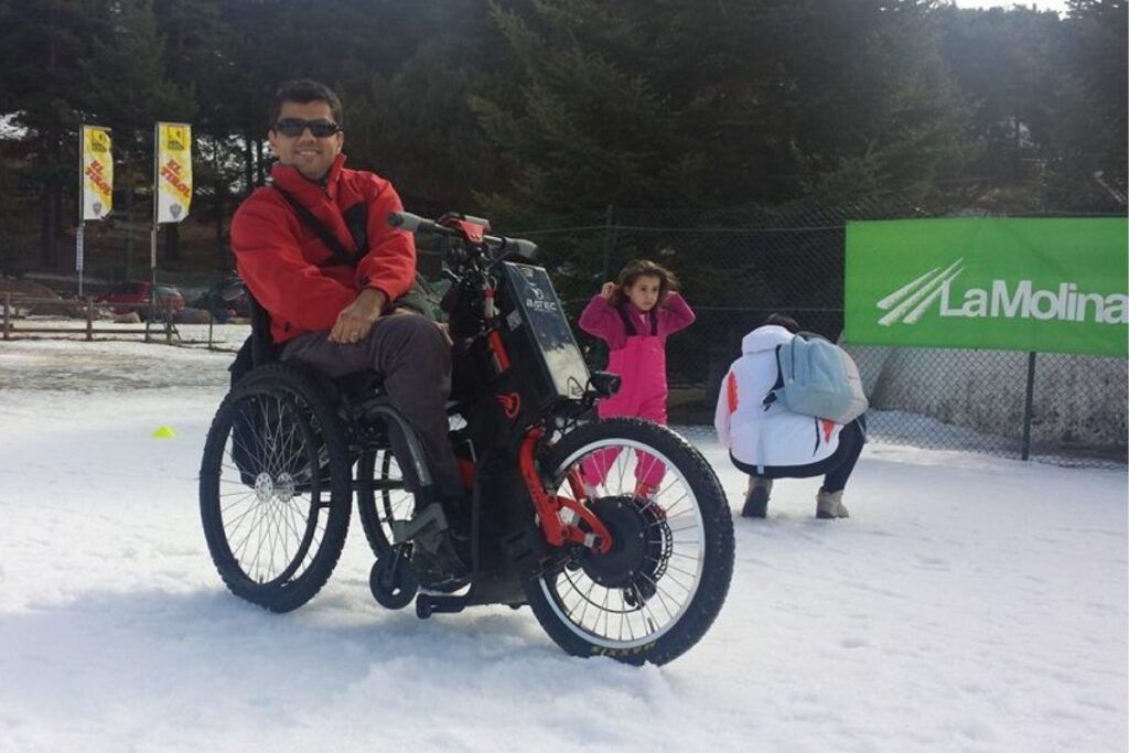 A wheelchair user with a Batec Mobility device at La Molina ski resort, ready to practise adapted skiing on a sunny, snowy day.