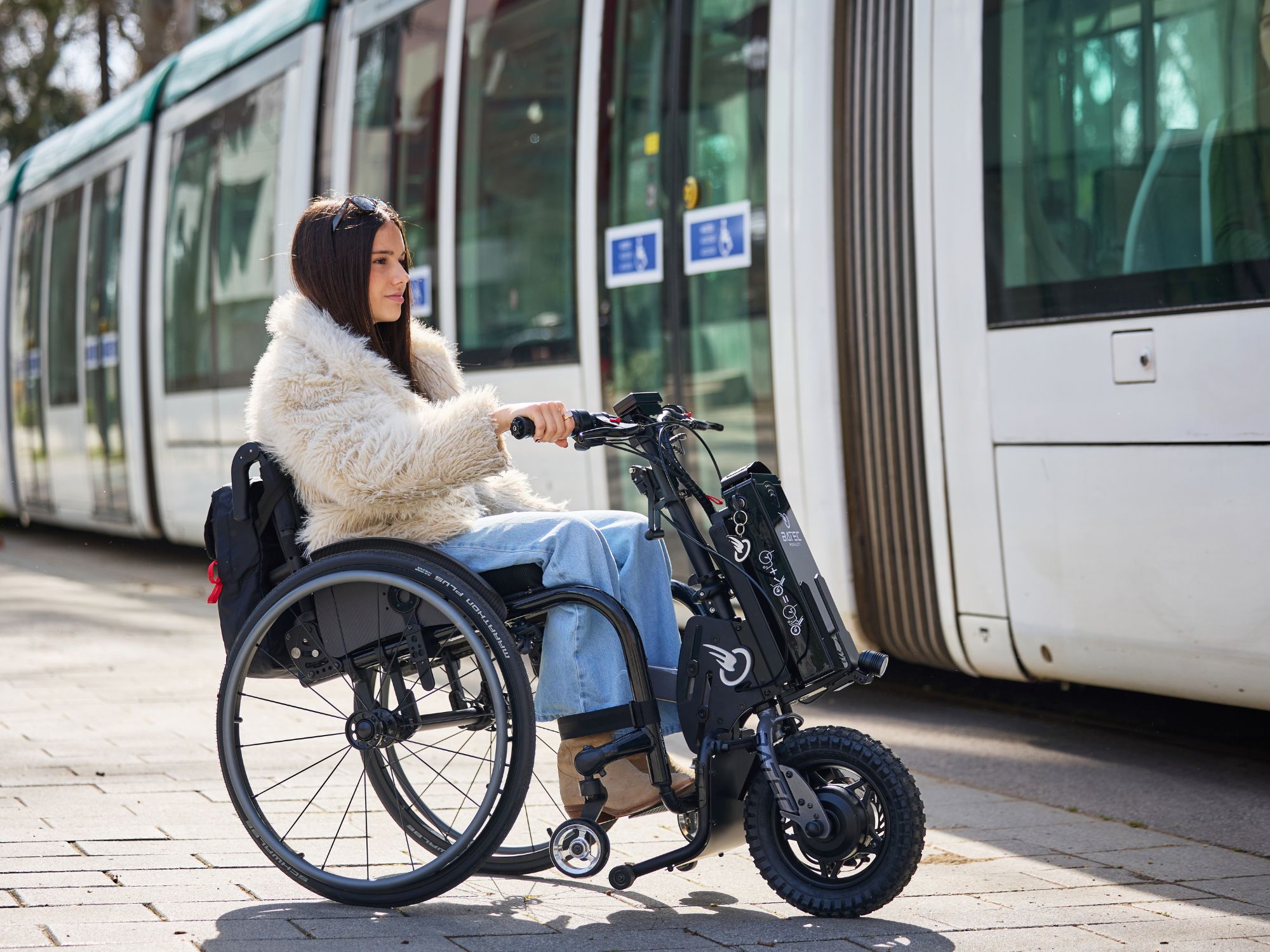 Wheelchair user with an electric handbike by a tram.