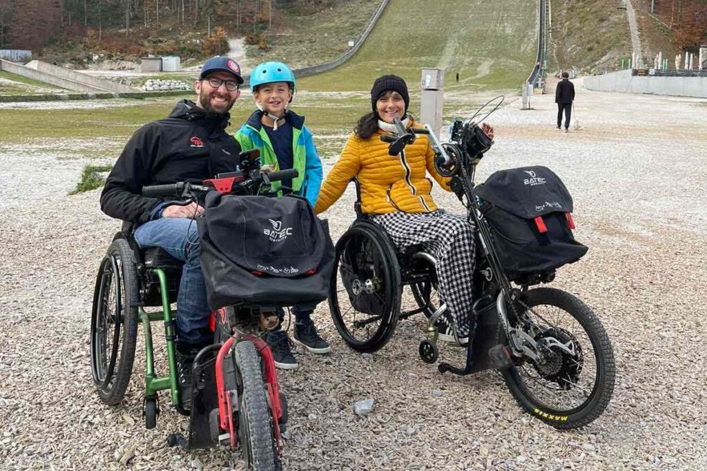 Matrimonio en silla de ruedas junto a su hijo. Están de vacaciones y el matrimonio lleva cada uno un handbike Batec. Refuerza la idea de que las personas que te acompañan disfrutan contigo sin preocuparse de ayudar.